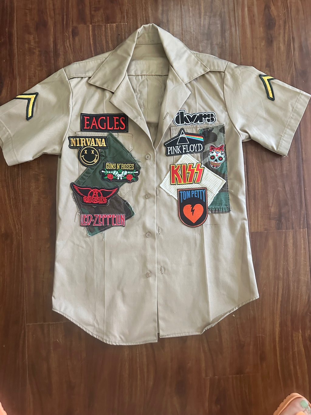 Lizzie Lee's Boutique khaki short sleeve button-up shirt with iconic band patches: Eagles, Nirvana, Guns N' Roses, Led Zeppelin, The Doors, Pink Floyd, KISS, Tom Petty.